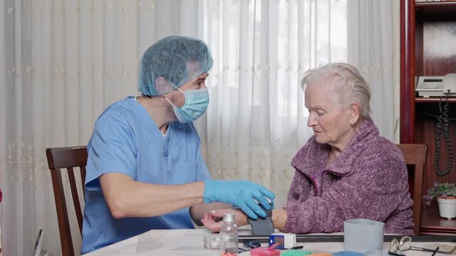 Caring medical professional checking a senior patient's health during a home visit, using a digital wrist tonometer and then giving her medication, highlighting elderly care and assistance