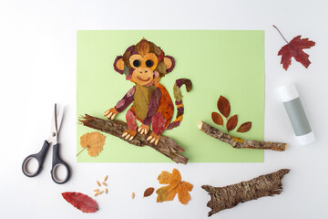 Monkey made from autumn leaves on branch with scissors and glue. Flat lay craft photography. Autumn nature and children creativity concept. Design for poster, print, greeting card, postcard © Elena