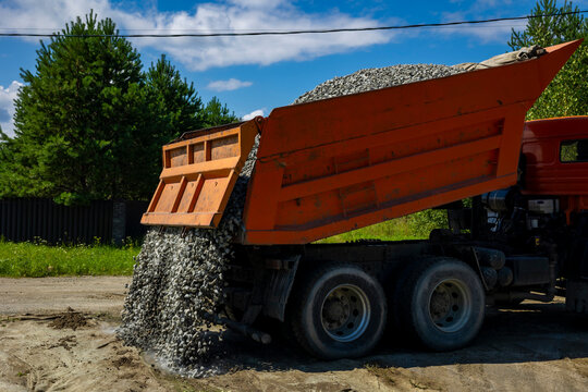 Orange dumper truck unloading crushed stone gravel on geotextile at construction site. Concept: aggregates supply industry