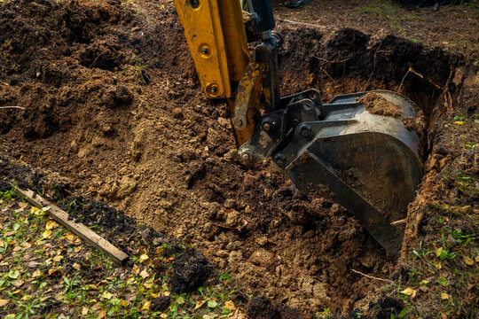 Yellow excavator bucket digging deep dirt trench for septic tank installation at backyard. Concept: septic tank installation