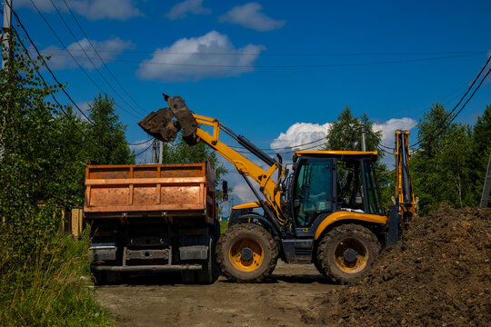Yellow backhoe loader filling dumper truck with dirt soil for site clearing. Concept: soil disposal service