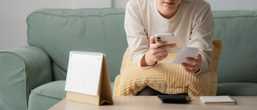 Personal budgeting concept. Anonymous person calculating household expenses with calculator while writing notes beside smartphone at home. Budget, finance, savings, planning, expenses