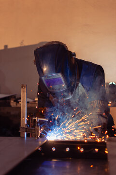 Frontal view of industrial welder wearing protective helmet while welding metal
