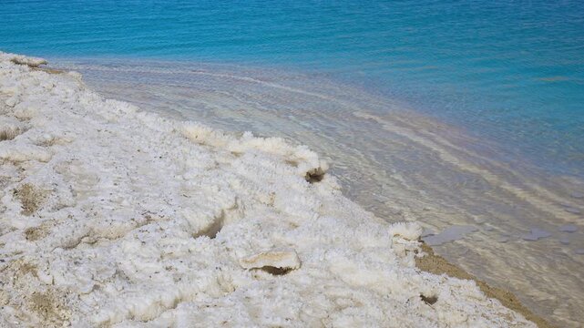 White crystalline salt formations at shore of Dead Sea on Jordan side, calm clear water near, closeup detail