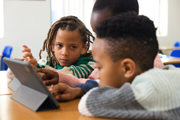Obraz premium African American children leaning in, gazing at tablet in folio on classroom table in sweaters