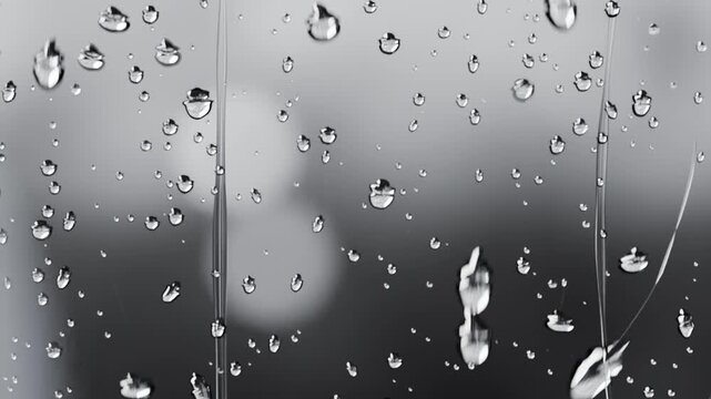 Sliding water droplets elongating and streaking down window pane with rain falling outside, bokeh