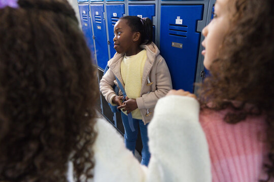African American teen females standing in school hallway holding blue folder by blue metal lockers