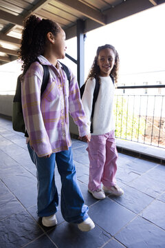 African American teen females walking holding hands along balcony with backpacks and white sneakers