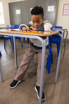 youth African student in sweater sitting in class at desk reading open book with yellow pencil