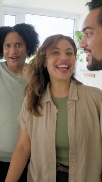 Vertical video: Recording phone filming three adults greeting camera in home kitchen, beige top