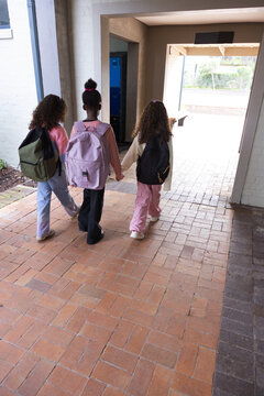 African American female students walking school hall holding hands and backpacks to courtyard