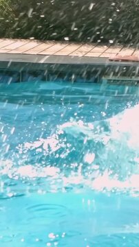 Vertical video: At edge woman jumping tucking into backyard pool in bikini making splash for fun