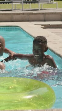 Vertical video: Youth reaching splashing climbing on adult in pool playing in red trunks green ring