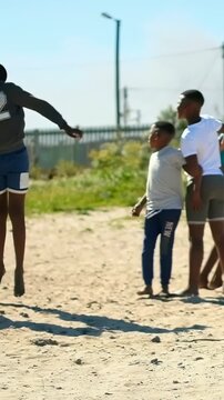 Vertical video: Running up, kicker in green top sending soccer ball across sand lot, boys playing