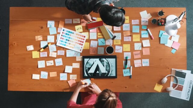 Top view of designer writing idea on colorful sticky notes while sitting at meeting table with tablet display logo design. Professional business woman looking design and making a decision. Symposium.