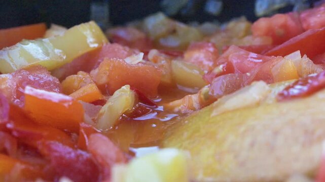Close-up video of a hand seasoning a colorful vegetable stew with a handful of fresh green herbs like oregano or basil in a hot frying pan.
