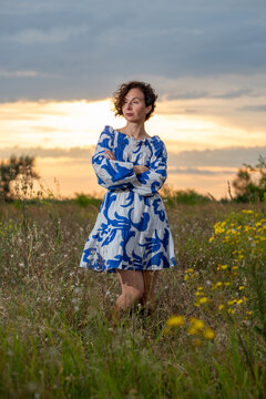 Woman in Blue Dress Standing in Wildflower Field at Sunset