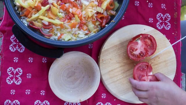 High angle close-up video of colorful sliced bell peppers, onions, and tomatoes simmering in a hot pan with a wooden spoon in the center. Fresh homemade vegetable meal.