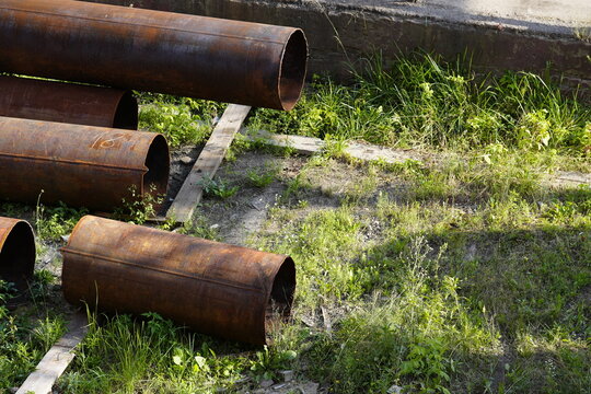 Rusty steel pipes stored outdoors on grass, showing metal corrosion, aging industrial materials and infrastructure maintenance