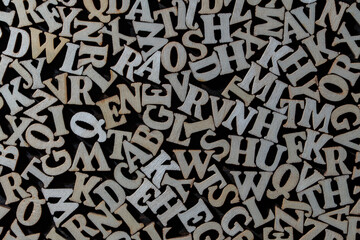 Abstract texture of wooden alphabet letters scattered on dark background, closeup. Top view of chaotic pile of wooden letters for education learning dyslexia or typography concept © OlegD