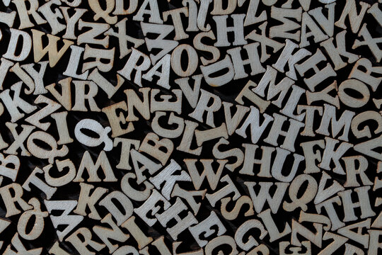 Abstract texture of wooden alphabet letters scattered on dark background, closeup. Top view of chaotic pile of wooden letters for education learning dyslexia or typography concept