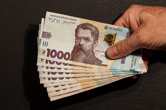 Hand holding fan of Ukrainian one thousand hryvnia banknotes. Closeup of male hand counting cash money paper bills of national currency of Ukraine 1000 uah, financial and economic concept