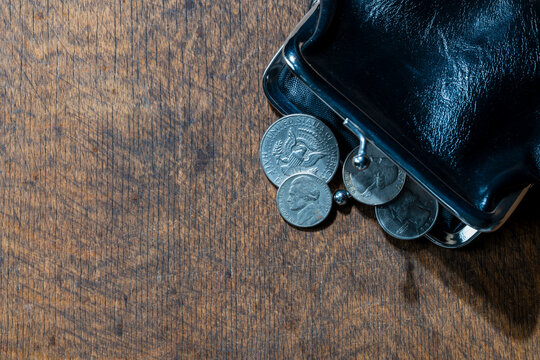 Vintage leather coin purse with US dollar coins on wooden background. Open black wallet with spilled american change cents and half dollar on table finance and budget concept with copy space