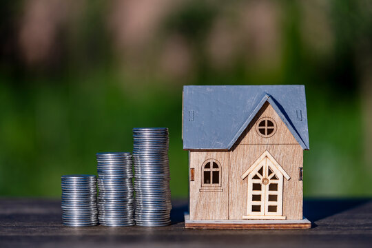 Wooden toy house next to rising stacks of coins. Concept real estate investment mortgage loan savings for property buying home insurance or finance growth with house model and silver coins