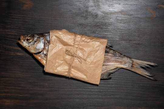 Dried salted fish wrapped in craft paper tied with twine. Top view of traditional stockfish roach wrapped in eco friendly brown paper on wooden background, beer snack food commercial concept