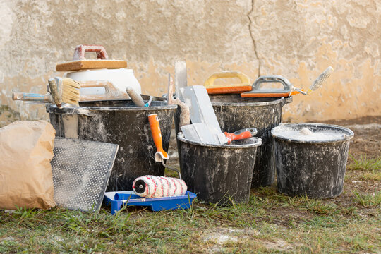 Construction buckets with plaster residue, trowels, paint roller and dry mix outdoors during home renovation and interior finishing work. Concept: home renovation, materials, prices and repair costs.