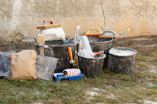 Construction buckets with plaster residue, trowels, paint roller and dry mix outdoors during home renovation and interior finishing work. Concept: home renovation, materials, prices and repair costs.