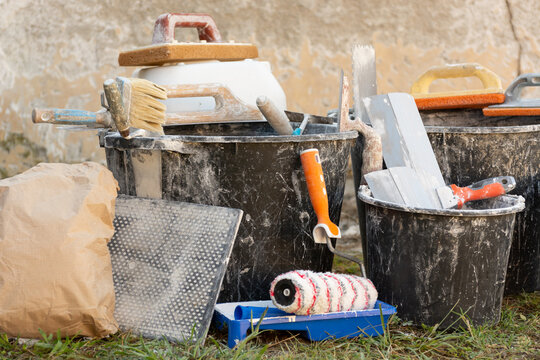 Construction buckets with plaster residue, trowels, paint roller and dry mix outdoors during home renovation and interior finishing work. Concept: home renovation, materials, prices and repair costs.