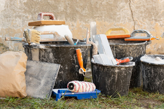 Construction buckets with plaster residue, trowels, paint roller and dry mix outdoors during home renovation and interior finishing work. Concept: home renovation, materials, prices and repair costs.