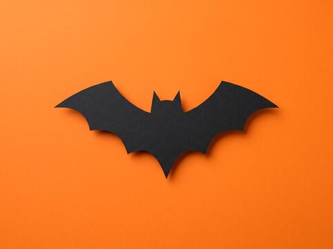 Single black paper bat cutout isolated on a vibrant orange background for halloween
