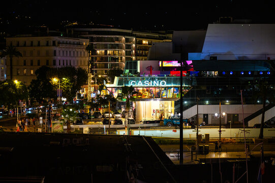 Cannes, France - July 29, 2026: An illuminated casino building stands prominently at night, surrounded by city lights, cars, and people