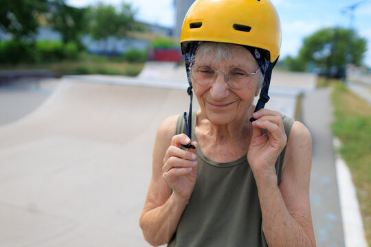 Elderly woman puts on helmet at skate park before skateboarding outdoors