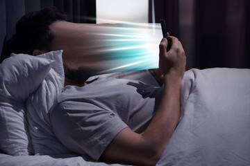Fototapeta premium Social media addiction consuming people's lives. Man using mobile phone in bed at night, his face being dragged into device