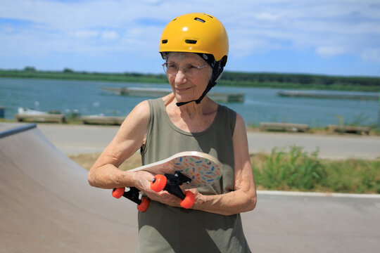 Elderly woman holds skateboard at skatepark near river on a sunny day