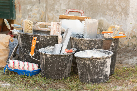 Buckets with plaster residue, trowels, paint roller and dry mix outdoors during home renovation and interior finishing work. Concept: home renovation, materials, prices and repair costs