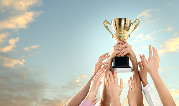 Winner with gold trophy cup and teammates reaching for it against beautiful sky, closeup. Space for text