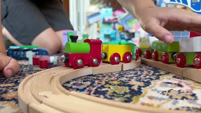 Child playing with wooden train cars on curved track over patterned rug in cozy playroom, hands arranging colorful pieces beside toy trees and buildings, with train, track, toy, wood detail