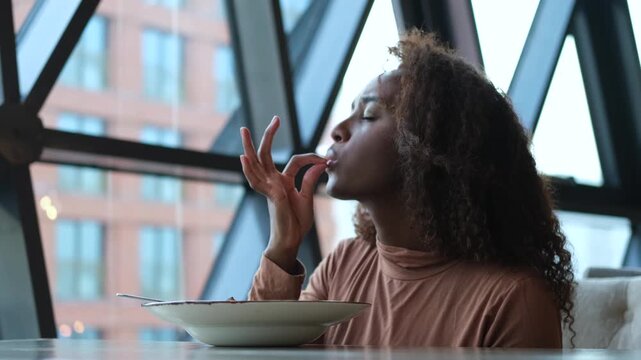 Beautiful African American woman eating pasta with seafood in a restaurant. Woman enjoying food. Close-up