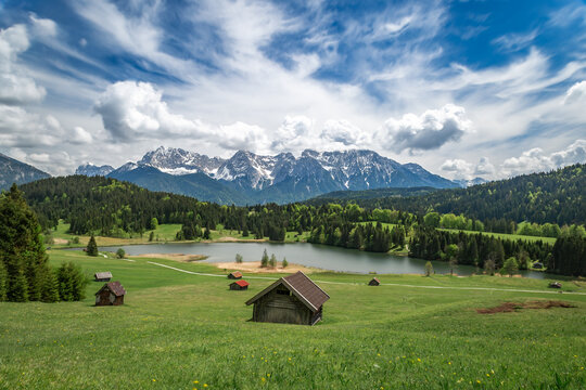 Small barns in Kr&uuml;n by lake Wagenbr&uuml;chsee surrounded by mountains and green fields. Cloudy skies provide a scenic backdrop.