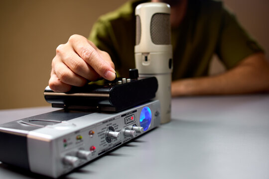 man adjusting settings on a professional audio interface in a focused studio environment with a green and black microphone and plastic and metal equipment close-up.