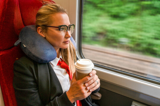 Woman sitting in a train holding a coffee cup while looking out at the scenery through the window