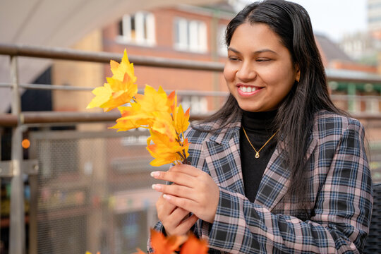 Young woman smiles while holding yellow leaves at an outdoor market on a clear day in autumn