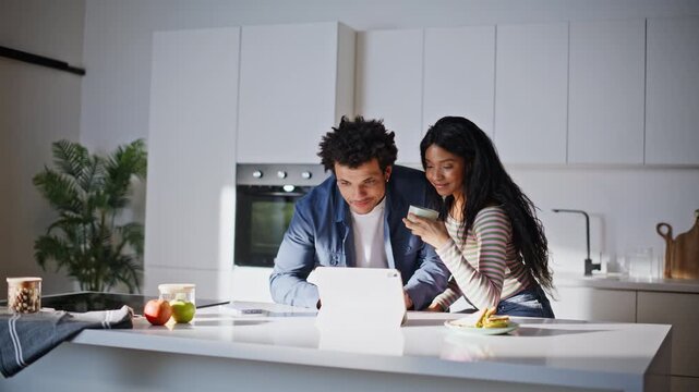 Smiling husband wife sipping espresso browsing computer bright kitchen closeup