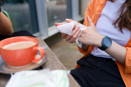 Person wipes hands with a napkin while sitting at a table with a coffee cup in a cafe