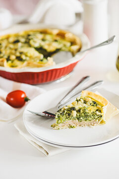 Freshly Baked Broccoli Quiche Slice on a Plate with Whole Quiche Background and Tomato