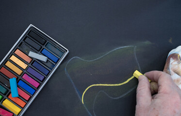 Hand drawing abstract shapes with yellow pastel chalk next to a box of colorful chalks © Floren Horcajo